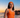 Woman in an orange swimsuit standing on a beach at sunset.