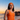 Woman in an orange swimsuit standing on a beach at sunset.