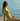 Woman in a green swimsuit sitting on a wooden dock by the water.