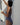 A woman wearing a one-piece swimsuit with a navy blue and white geometric circle pattern, photographed from behind against a white wall.