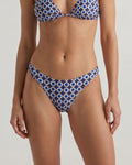 A model wearing a two-piece bikini with a blue, white, and black geometric circle pattern, shown from the chest to the upper thighs against a plain light gray studio background.